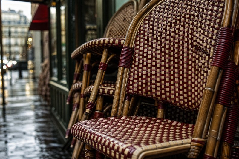 Close view of woven rattan bistro chairs in cream and red stacked outside a Paris café before opening